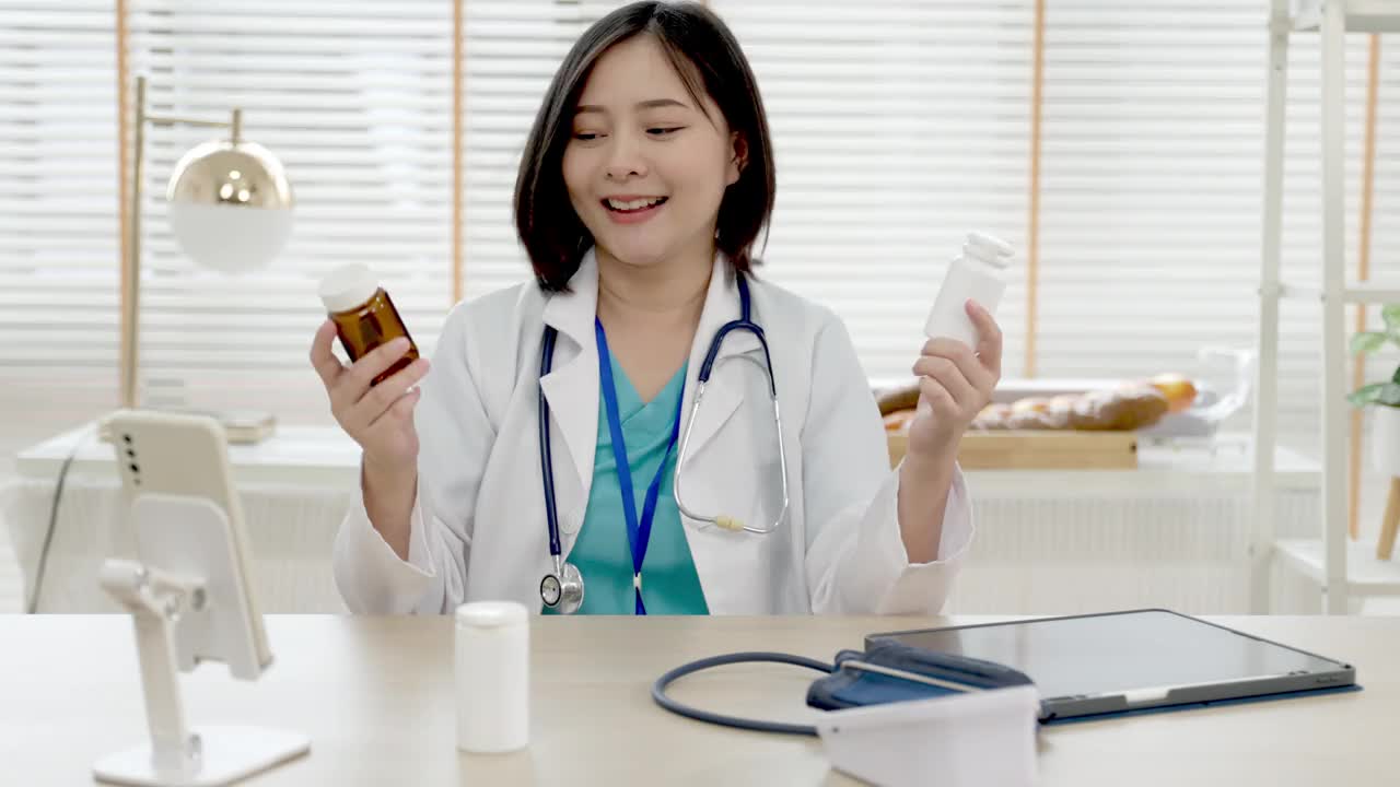 自信的年轻亚洲女医生穿着白色医疗制服，带着听诊器看着镜头，微笑着健康医院。一个微笑的医生在办公室的肖像。视频素材