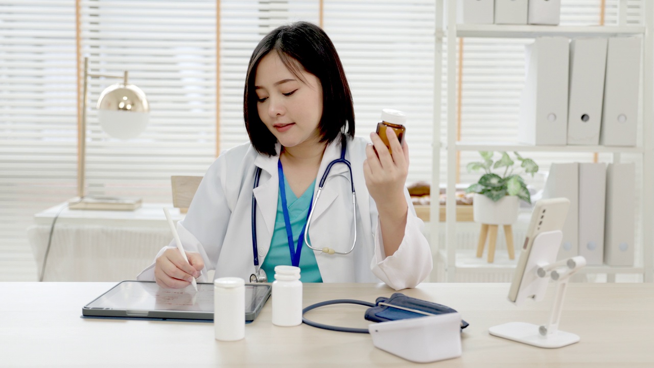 自信的年轻亚洲女医生穿着白色医疗制服，带着听诊器看着镜头，微笑着健康医院。一个微笑的医生在办公室的肖像。视频素材