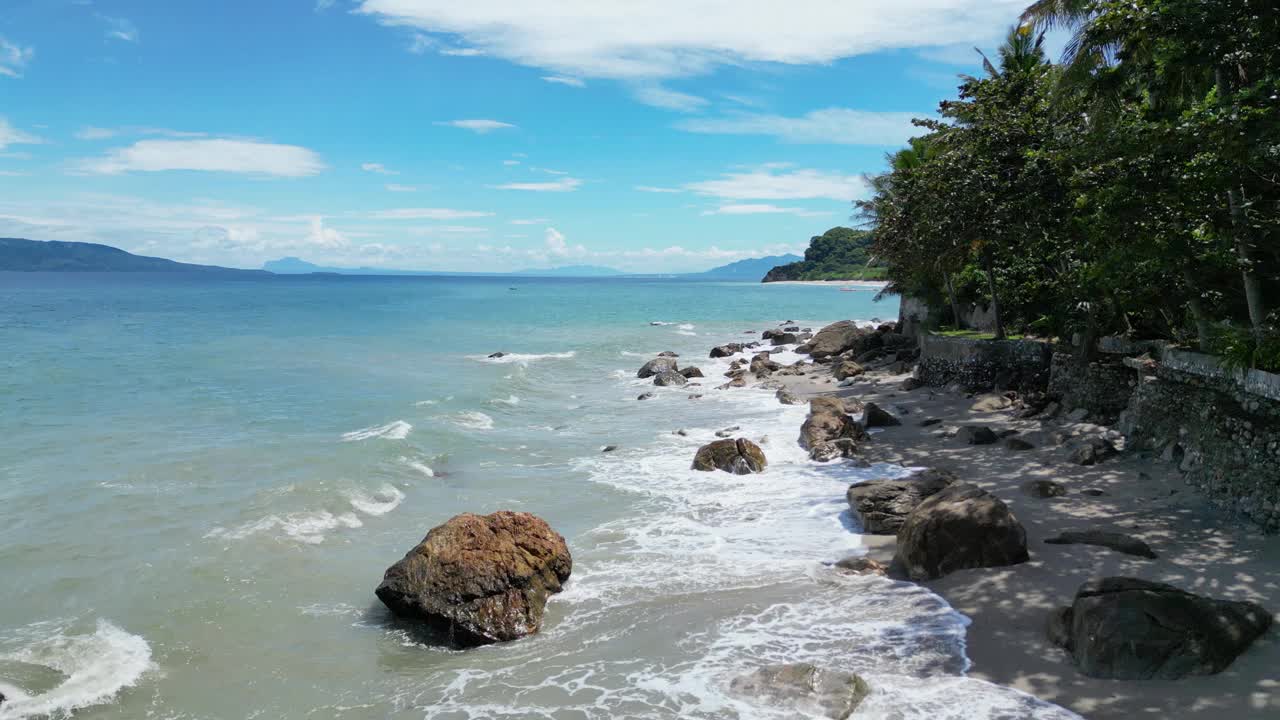 海滩上有被海水冲刷的岩石和海岸上的热带树木视频下载
