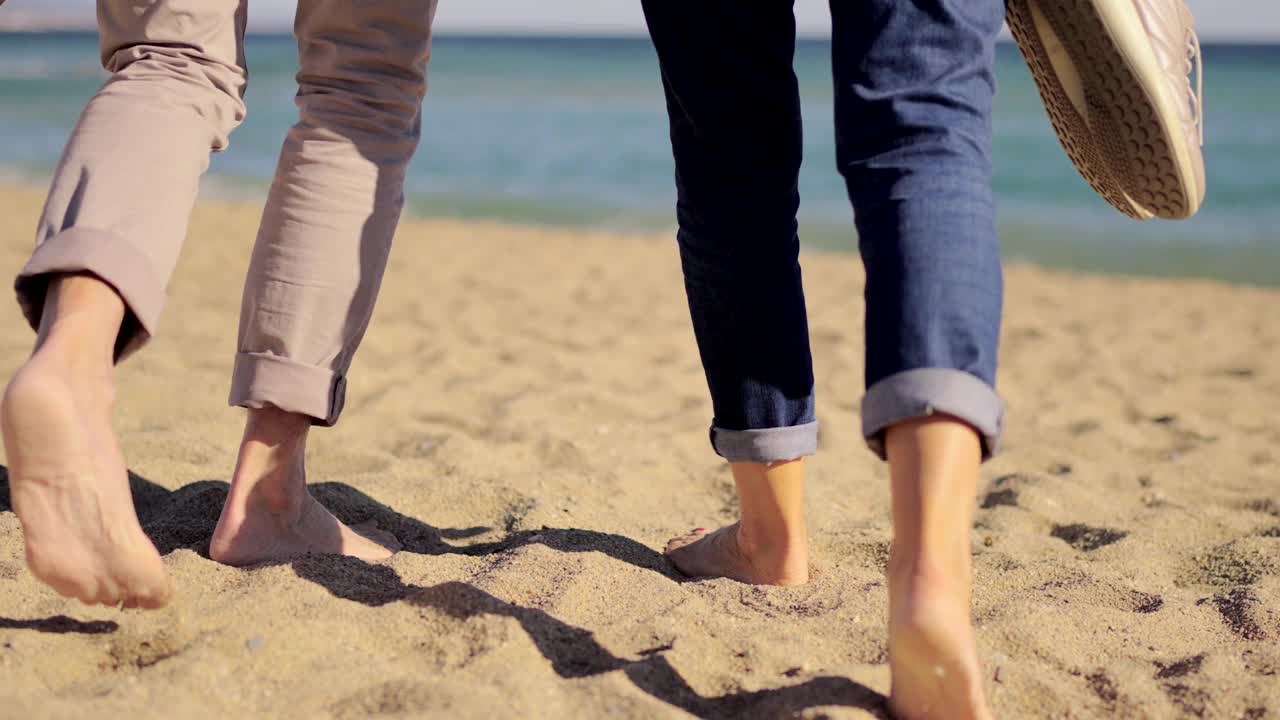 一对老年夫妇赤脚沿着海滩散步的后视图视频下载