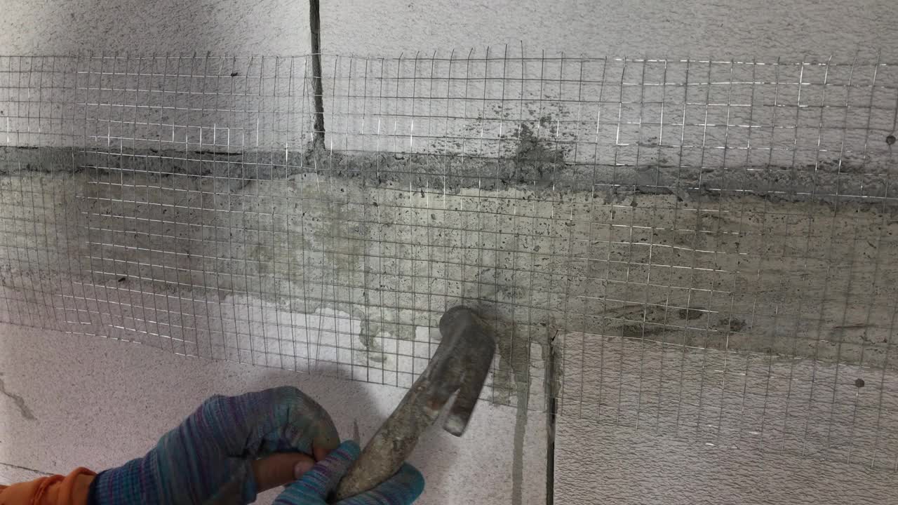 建筑工人在给轻质砖墙抹灰之前，正在把钉子钉进钢网。视频下载