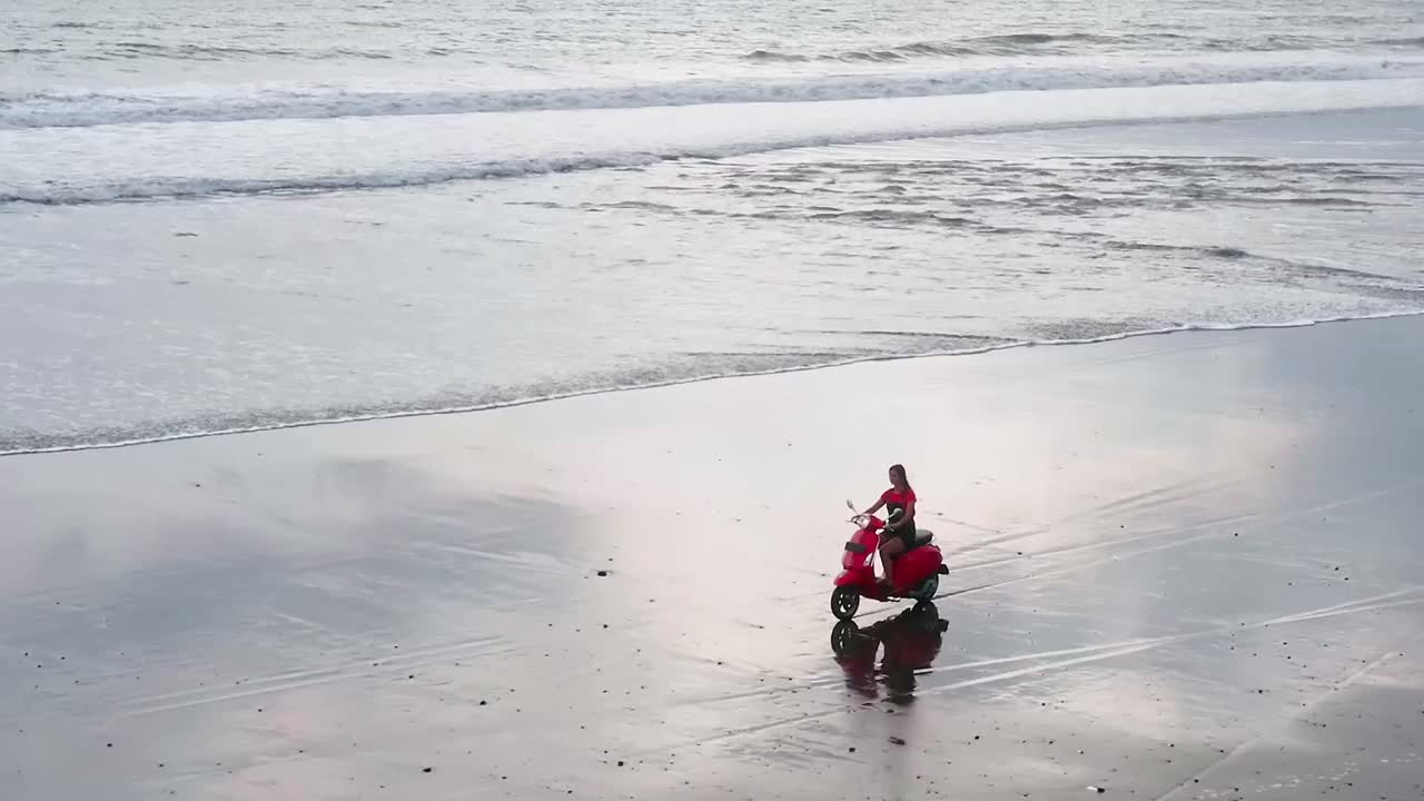 年轻女子穿着夏天的衣服，骑着老式的摩托车，在孤独的退潮海水白色的沙滩上视频下载
