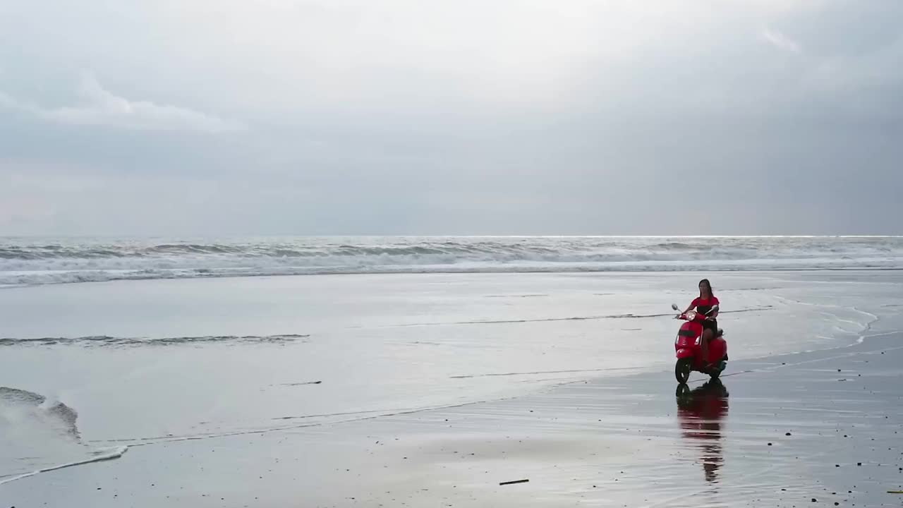 年轻女子穿着夏天的衣服，骑着老式的摩托车，在孤独的退潮海水白色的沙滩上视频下载