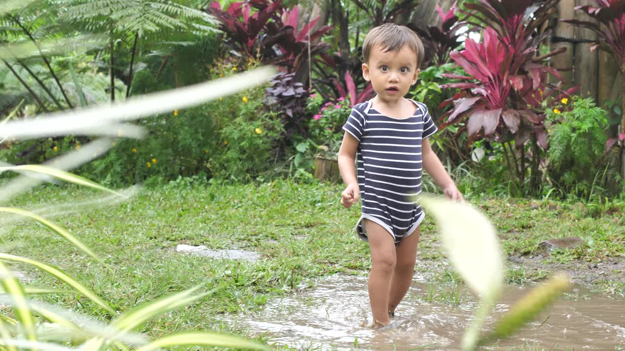 雨后，一个活泼的男孩穿着运动鞋走过院子里的水坑视频下载