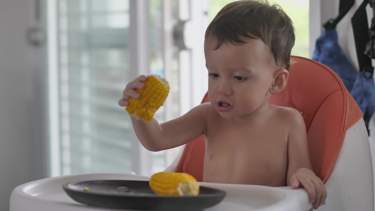 小孩坐在儿童高脚椅上玩煮熟的玉米视频下载