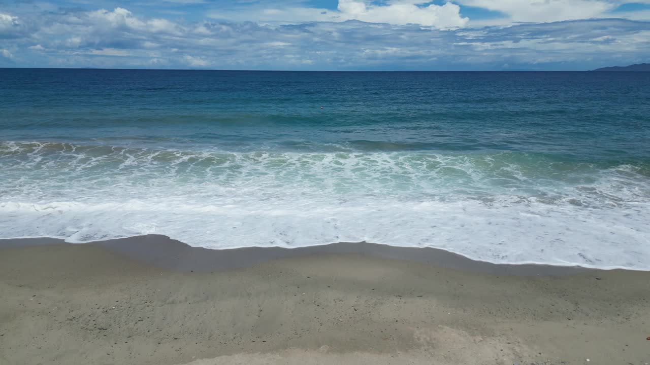 白天，海浪拍打着沙滩，映衬着乌云密布的天空视频下载