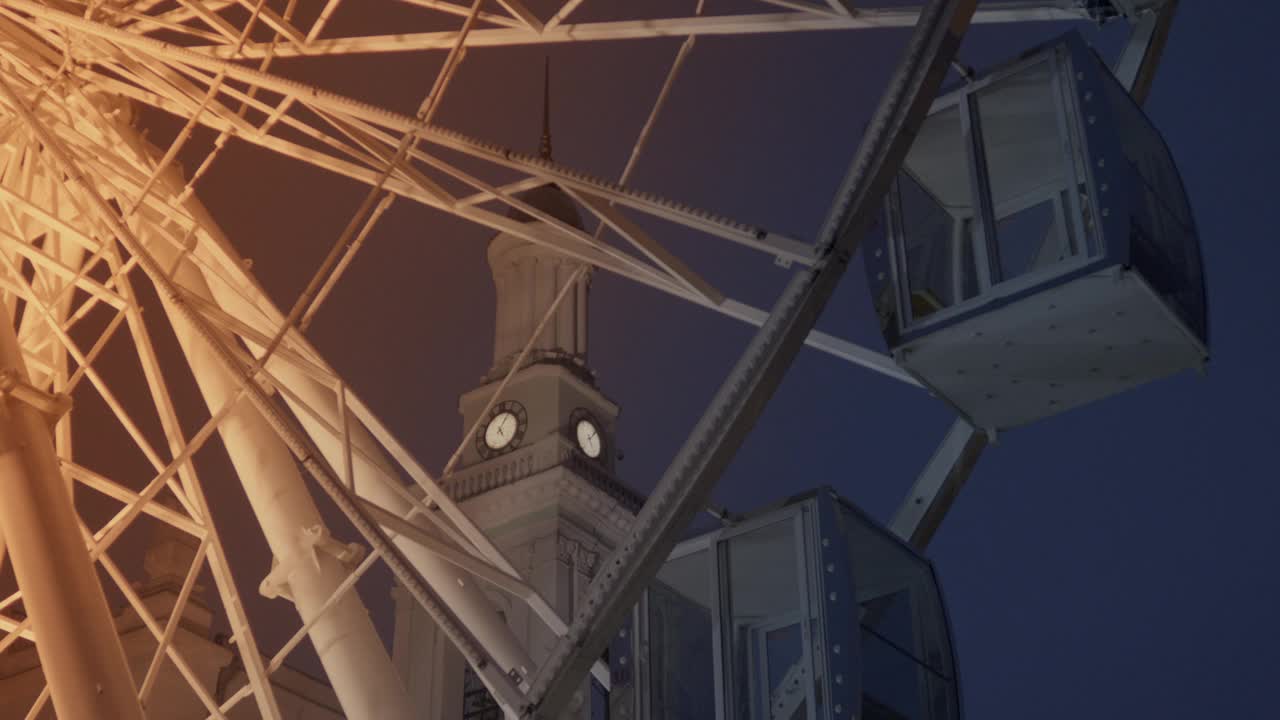 慢慢移动的摩天轮在钟楼上的特写，夜空视频下载