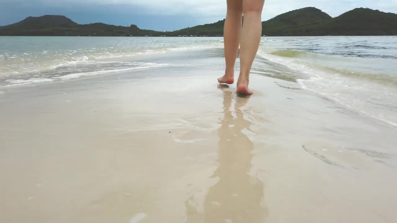 美丽的女人在日落时走在海边:一个低部分的场景视频下载