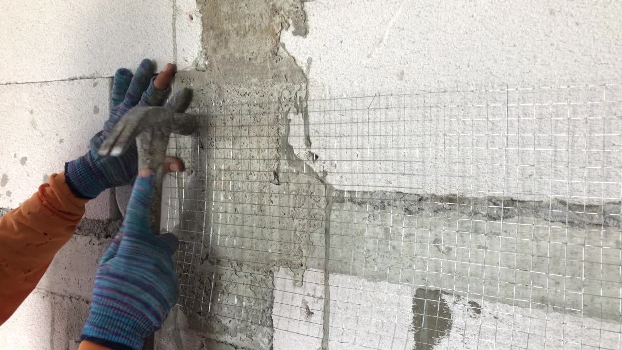 建筑工人在给轻质砖墙抹灰之前，正在把钉子钉进钢网。视频下载