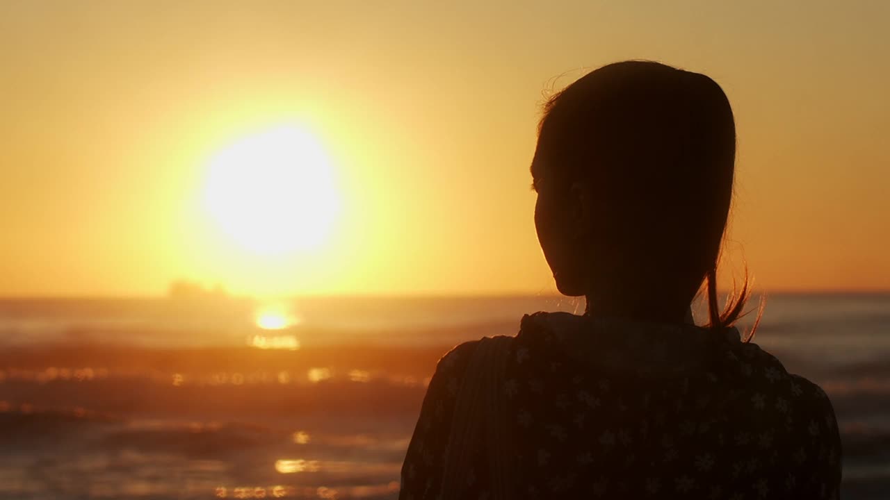 夕阳背景下一个女孩的剪影。傍晚散步时，海边的女人在欣赏一艘在海上航行的船。浪漫的心情和氛围视频下载