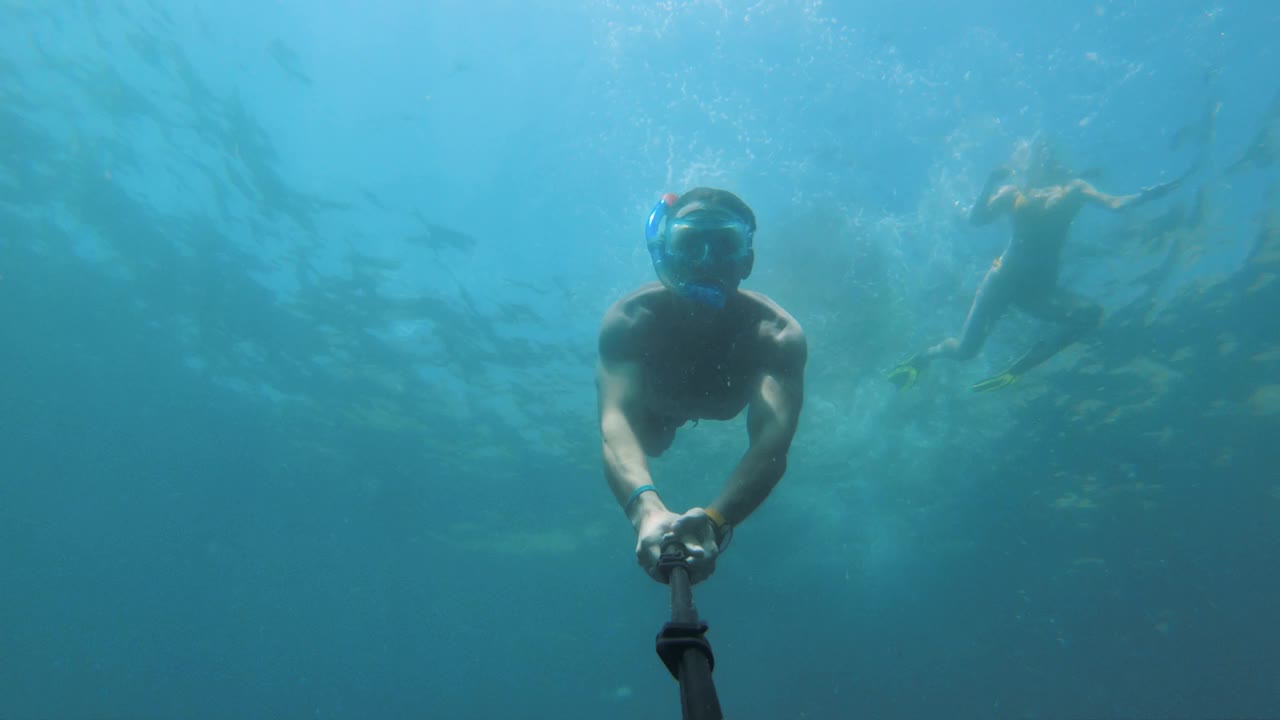 在一个阳光明媚的日子里，一名男子戴着带呼吸管的面具在水下游泳，一边自拍，一边在海上放松视频素材