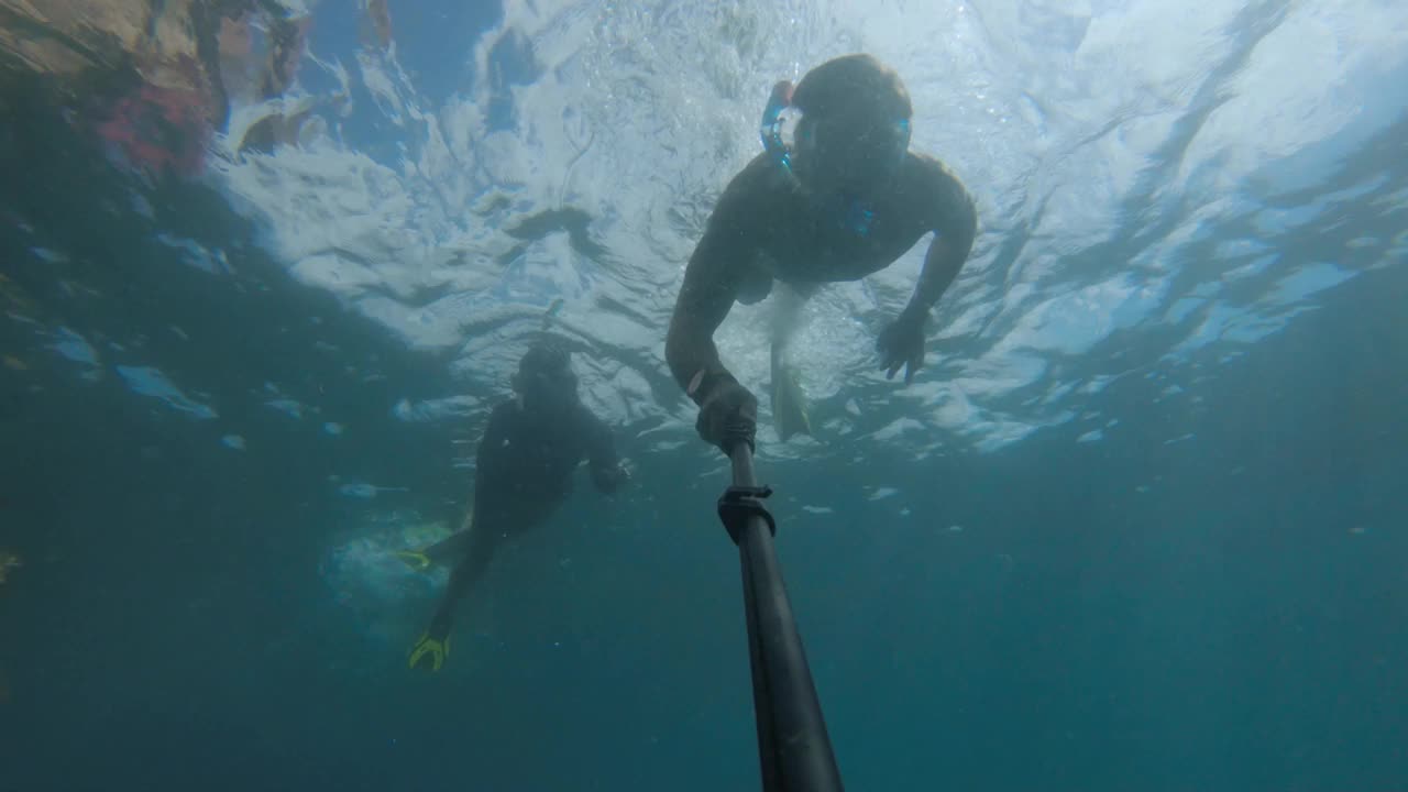 一名男子戴着面具在水下游泳，白天在海底自拍，漂浮在一艘被藻类覆盖的沉船的空中视频素材