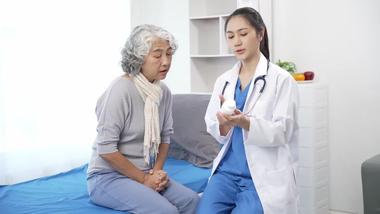 亚洲护理护士在病床上检查老年亚洲女病人。有吸引力的照顾者支持，提供建议和咨询与老年祖母在诊所。4 k 60 p视频下载