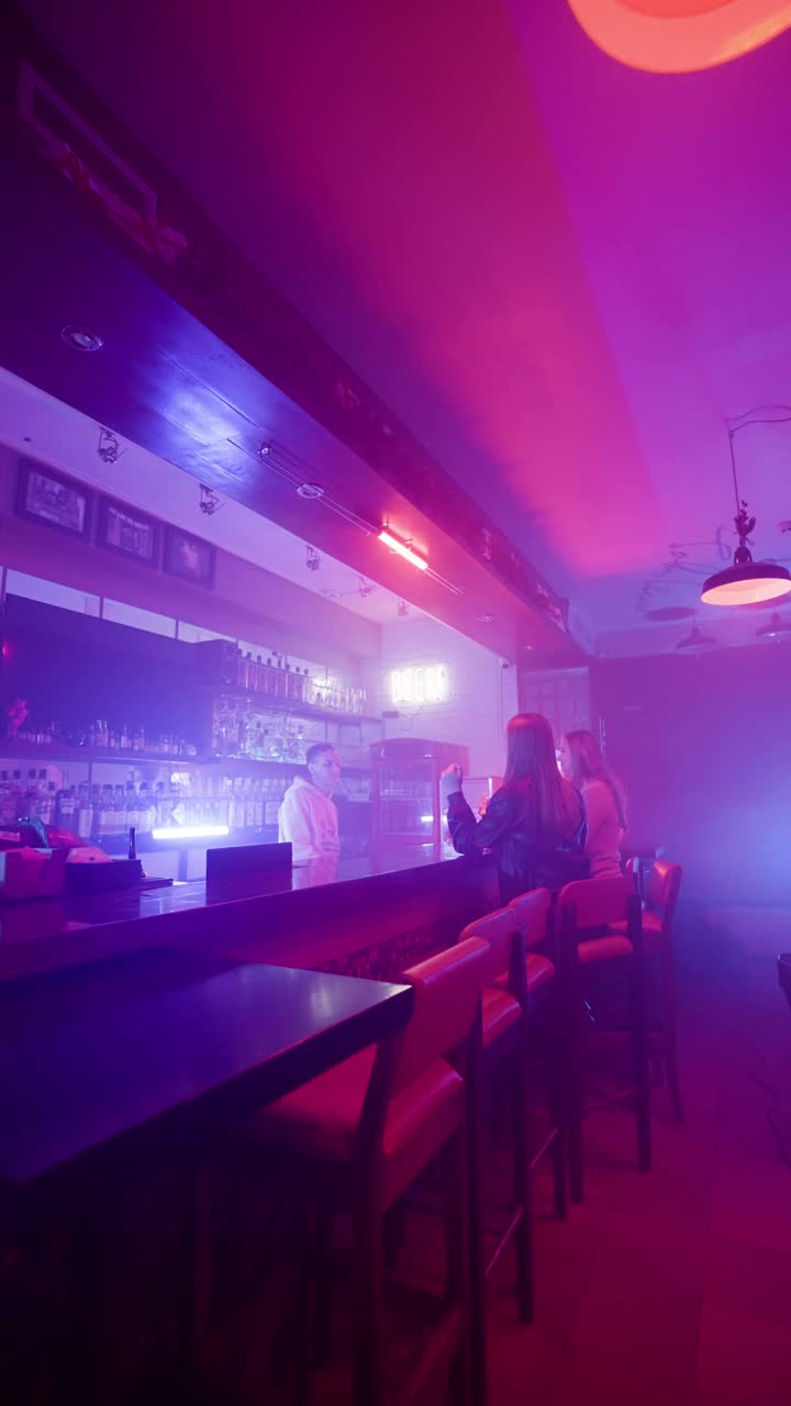 两个女人在酒吧里和酒保谈话。紫色和蓝色霓虹灯视频下载