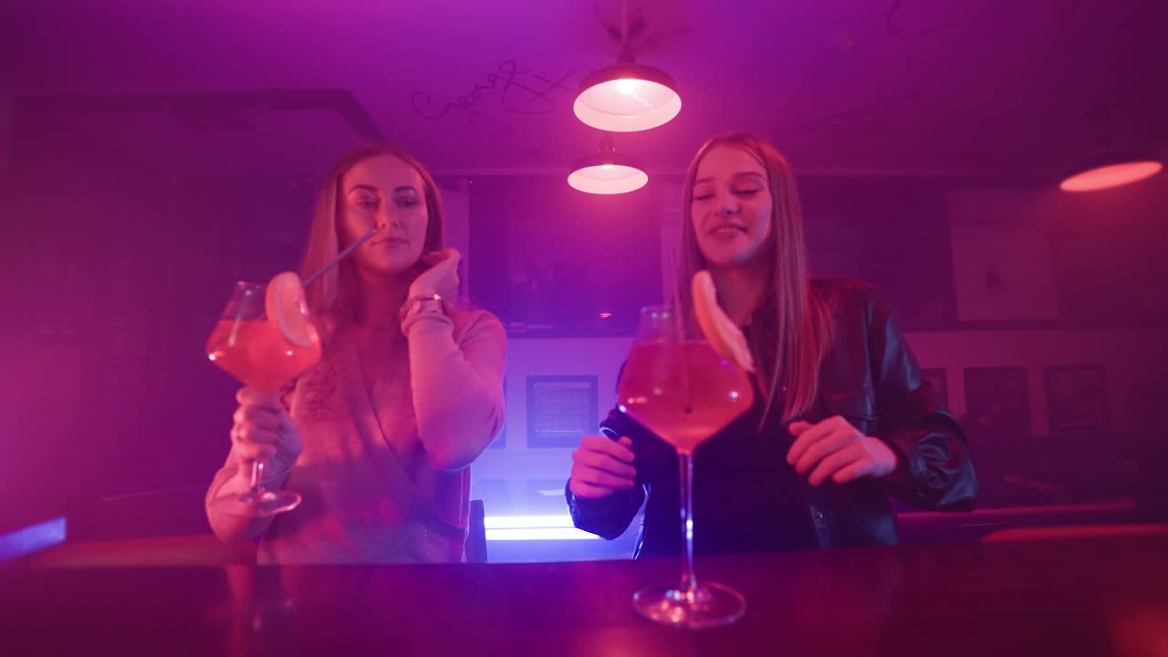 两个女朋友在霓虹灯夜总会里手拿鸡尾酒跳舞视频下载
