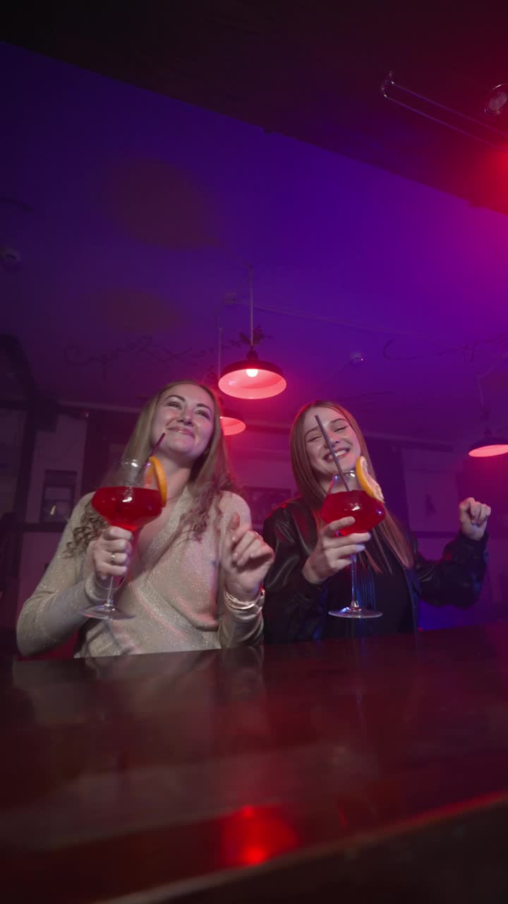两个女朋友在霓虹灯夜总会里手拿鸡尾酒跳舞视频下载