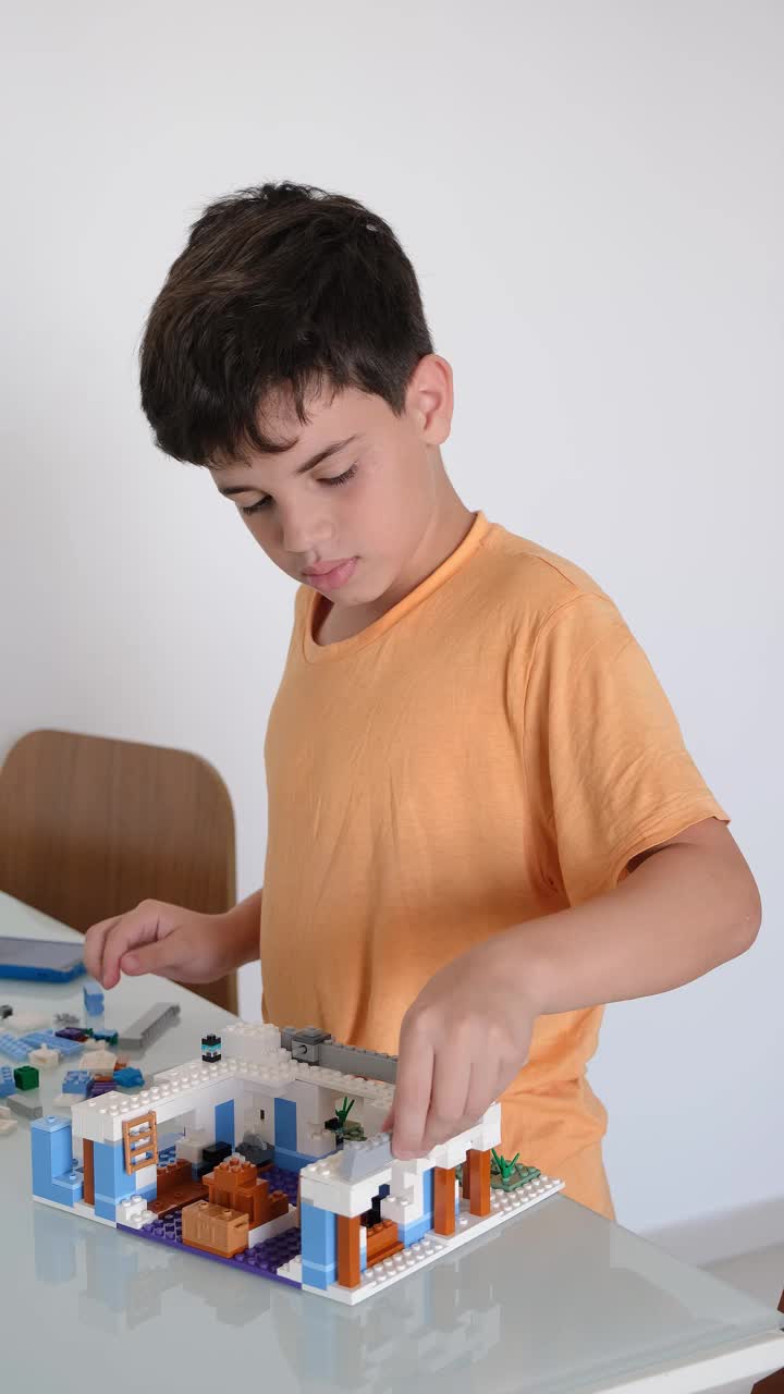 一个10岁的孩子一边玩积木，一边看智能手机上的在线手册。视频下载