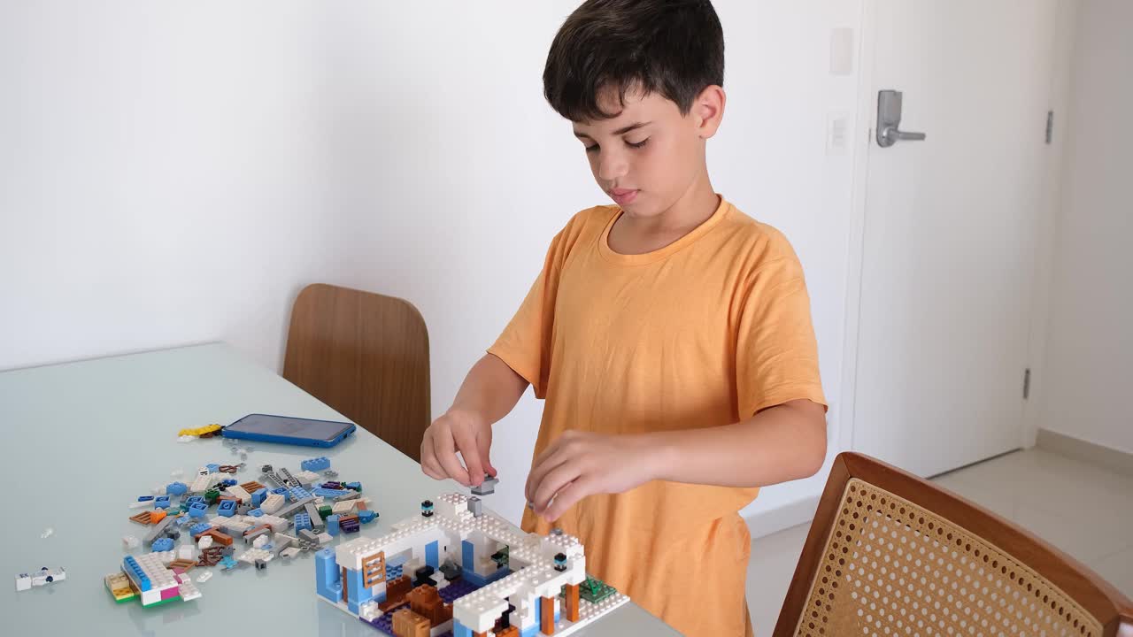 一个10岁的孩子一边玩积木一边看智能手机上的在线手册。视频下载