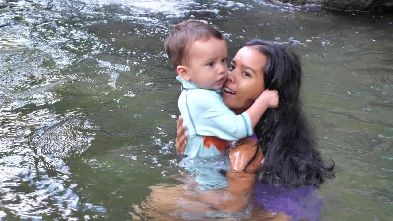 年轻的母亲带着小儿子在清澈的河水中游泳视频下载