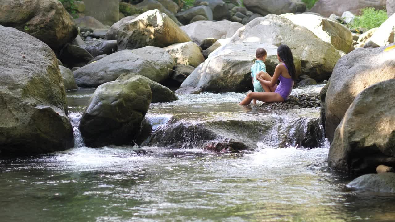 年轻女子带着小孩在岩石河的激流中洗澡视频下载