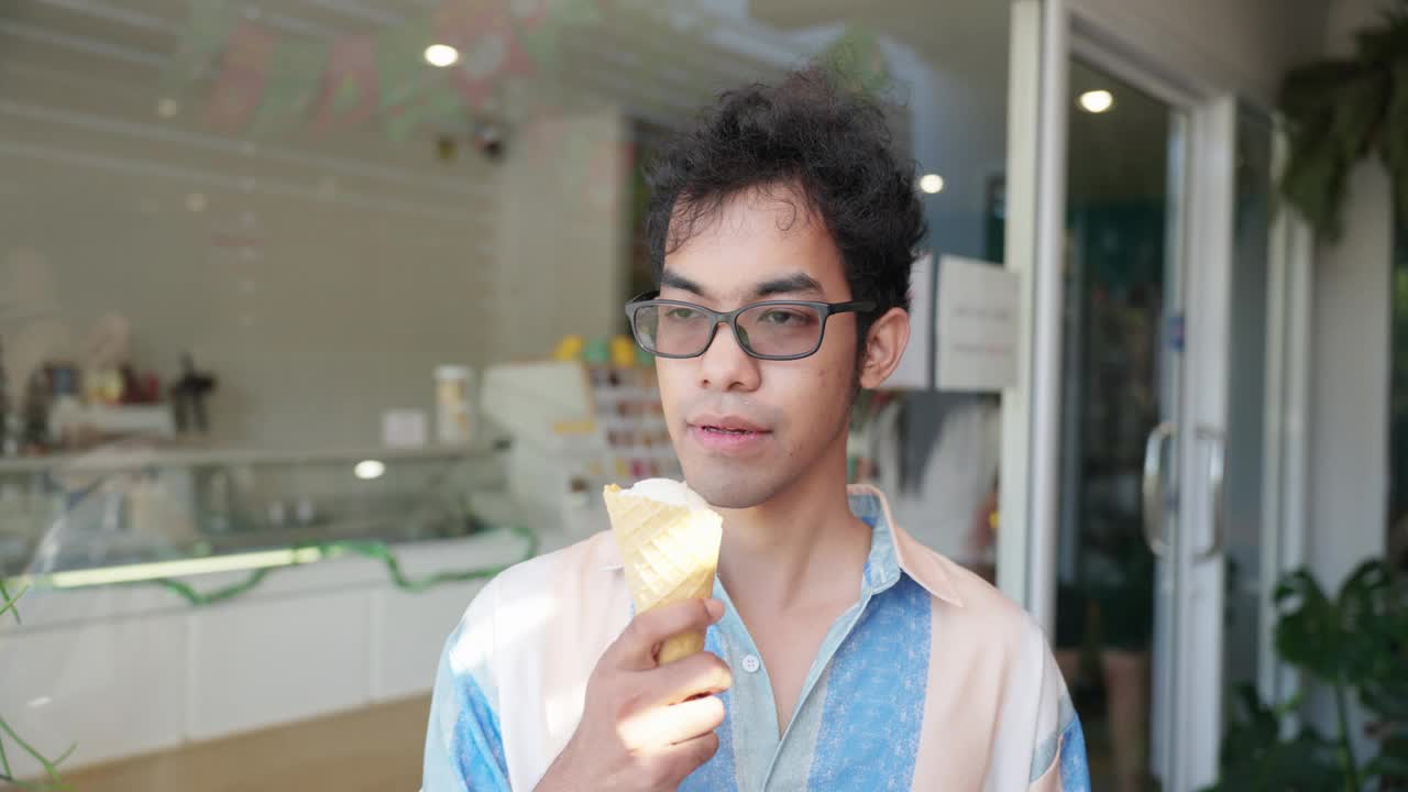 中年成年亚洲男子，穿着休闲服装，戴着眼镜，用手按摩脸颊，原因是在咖啡馆吃了冰淇淋蛋筒后牙痛。中年成年亚洲男性手捧美味的冰淇淋，吃完冷甜点后面部疼痛视频下载