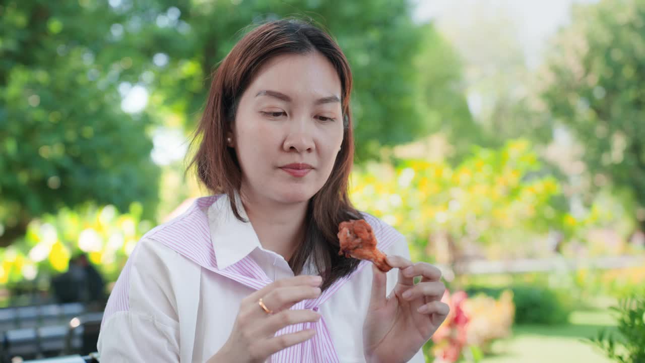 亚洲中年女性在吃了美味的烤鸡后，咬了鸡的硬骨头，感到牙痛。美丽的女孩吃烤鸡时牙疼。敏感的牙齿。视频下载