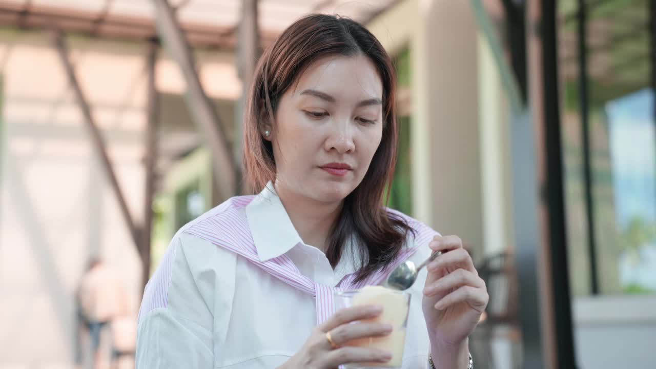 中年成年美丽的亚洲妇女穿着休闲布用勺子吃冰淇淋，以保护和避免牙齿疼痛的低温甜点和食物。亚洲女性因牙痛而表示疼痛并触摸她的脸颊。视频下载