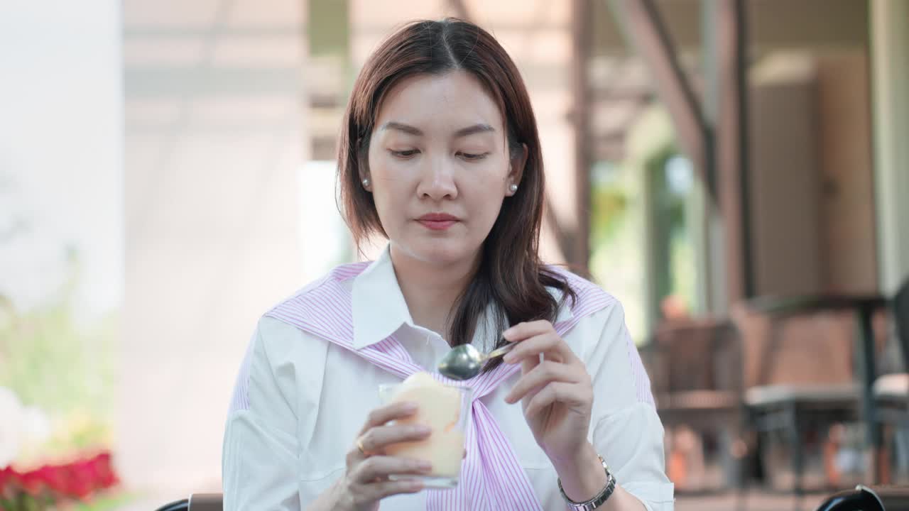 牙痛的亚洲中年女孩手里拿着一杯冰淇淋。亚洲女性穿着随意的衣服，吃着冷饮，用敏感的牙齿疼痛来表达不好的情绪。牙釉质过敏和牙齿健康问题。视频下载