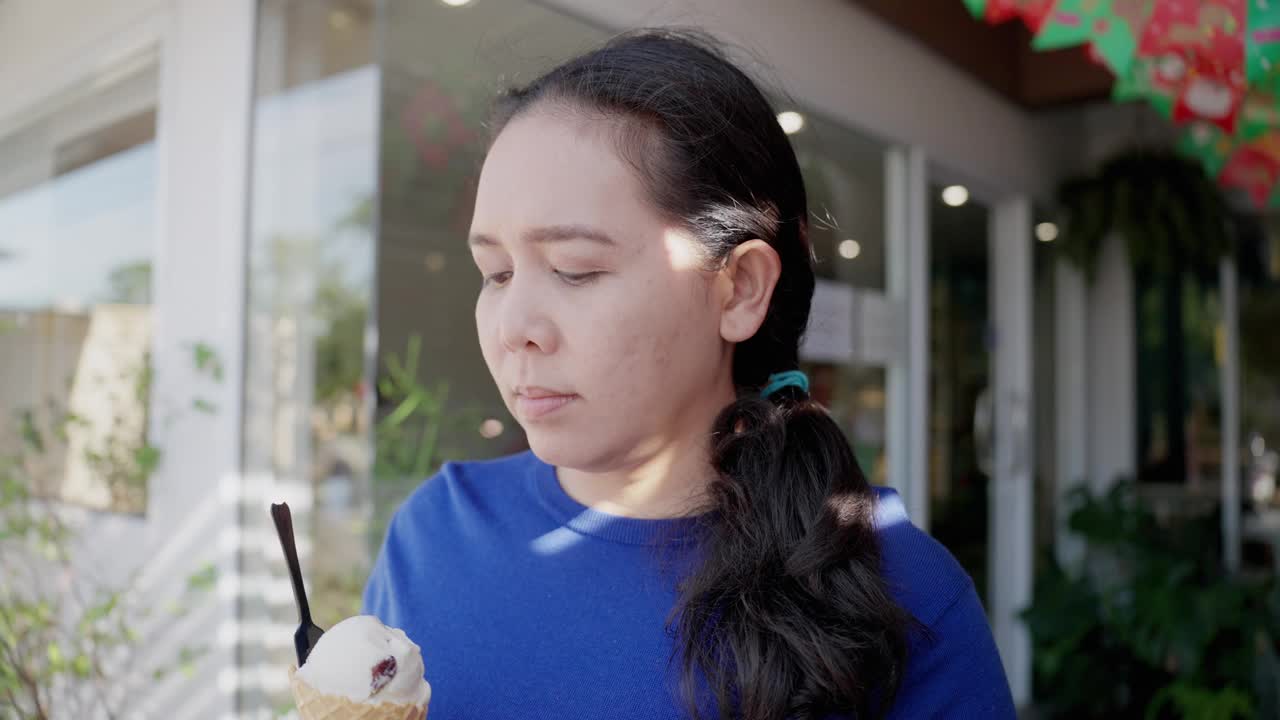 中年亚洲美女在咖啡馆吃冰淇淋后牙痛，试图用小勺子舀冰淇淋来避免和保护。她手里拿着一个甜筒冰激凌，感到一阵剧痛。牙龈萎缩，牙齿护理。视频下载