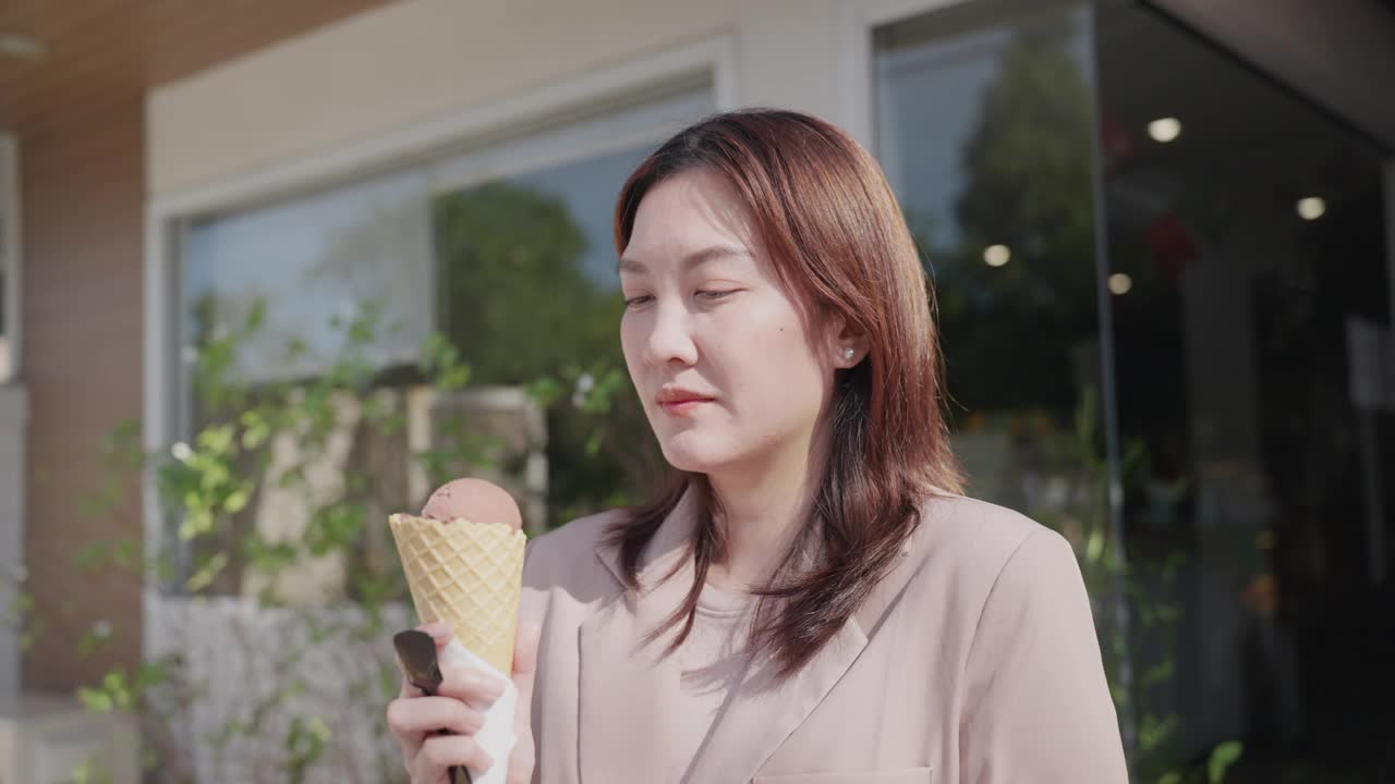 亚洲中年妇女吃完冰淇淋后牙疼得厉害。美丽的亚洲女性站在冰淇淋店前，抚摸着自己的脸颊，感觉受到了伤害，患有敏感的牙痛。疼痛和蛀牙。视频下载