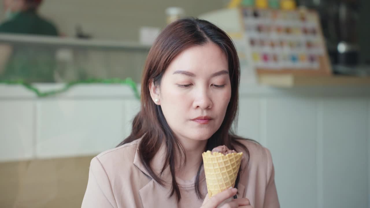 穿着粉色运动夹克的成年亚洲女性为了保护牙齿敏感，用勺子从威化筒里舀冰淇淋。亚洲女性吃冷甜点后牙痛，用手按摩脸颊。牙龈萎缩，牙齿护理。视频下载