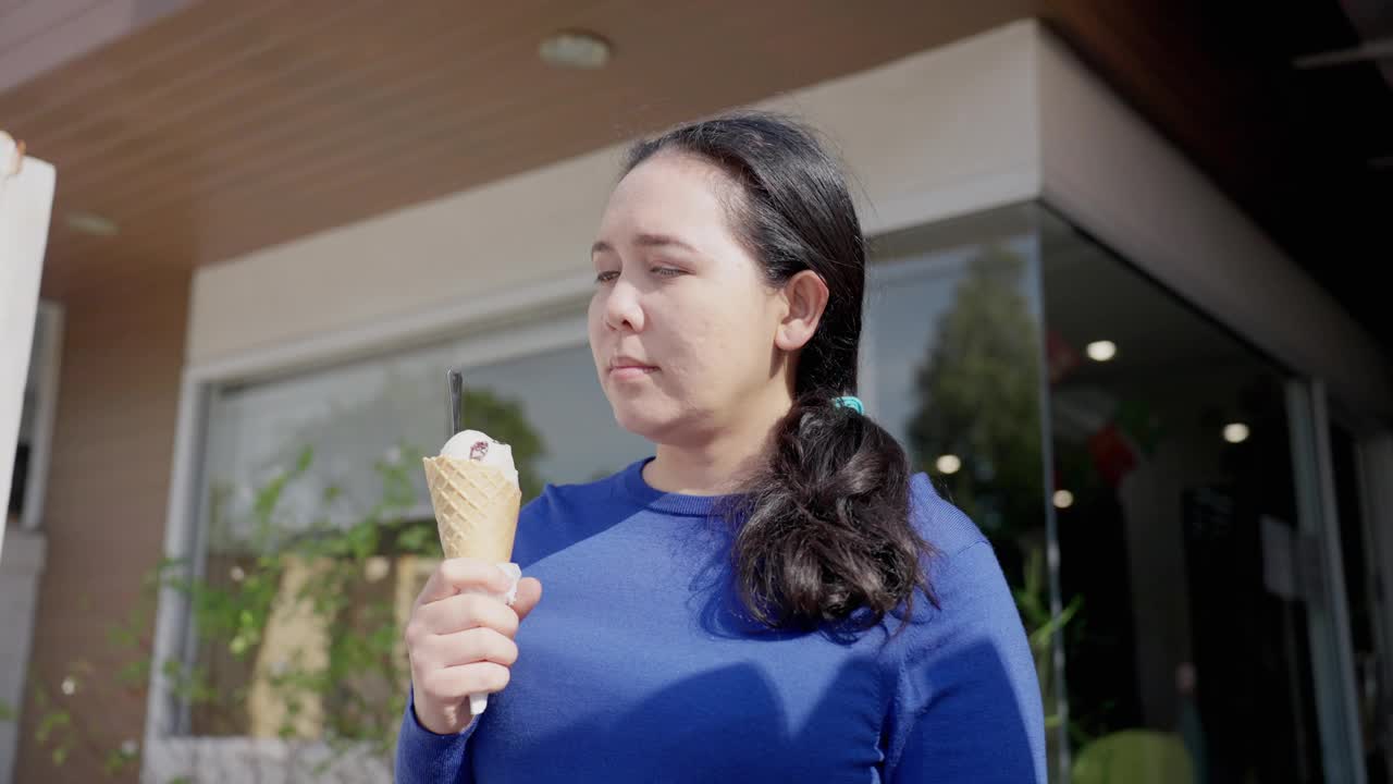 穿着蓝色t恤的亚洲中年女性喜欢去咖啡馆买美味的冰淇淋，但吃完冰尖叫后，尽管用小勺子，她还是感到牙痛和疼痛。牙龈萎缩，牙齿护理。视频下载