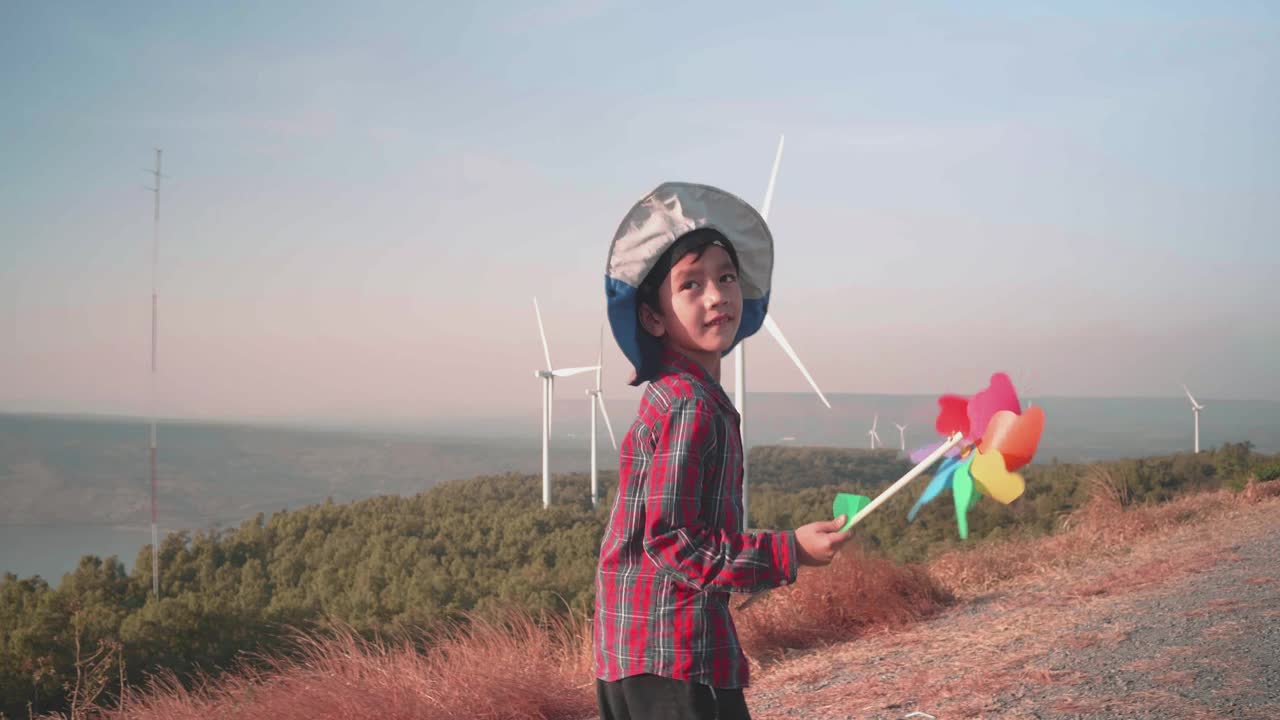 快乐的男孩在风力涡轮机旁玩风车。视频下载