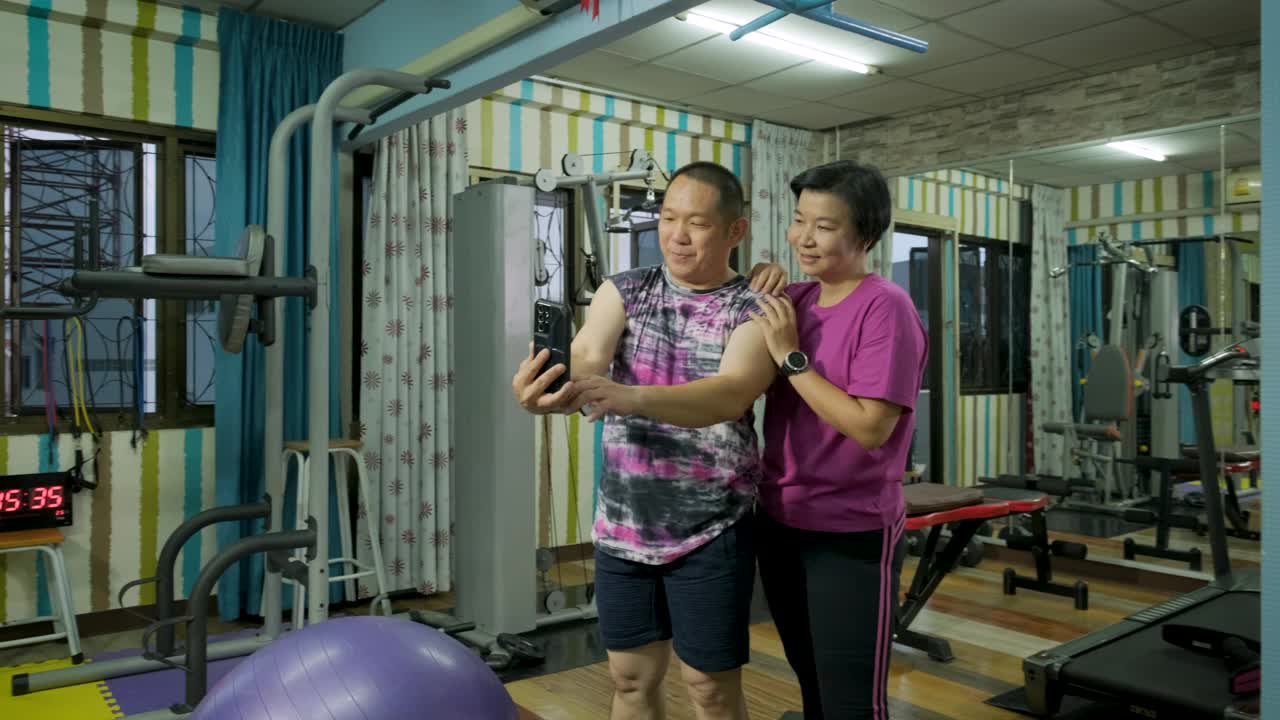 亚洲成熟夫妇在家里的健身房或健身俱乐部一起进行力量训练和身体锻炼后用手机自拍的照片视频下载