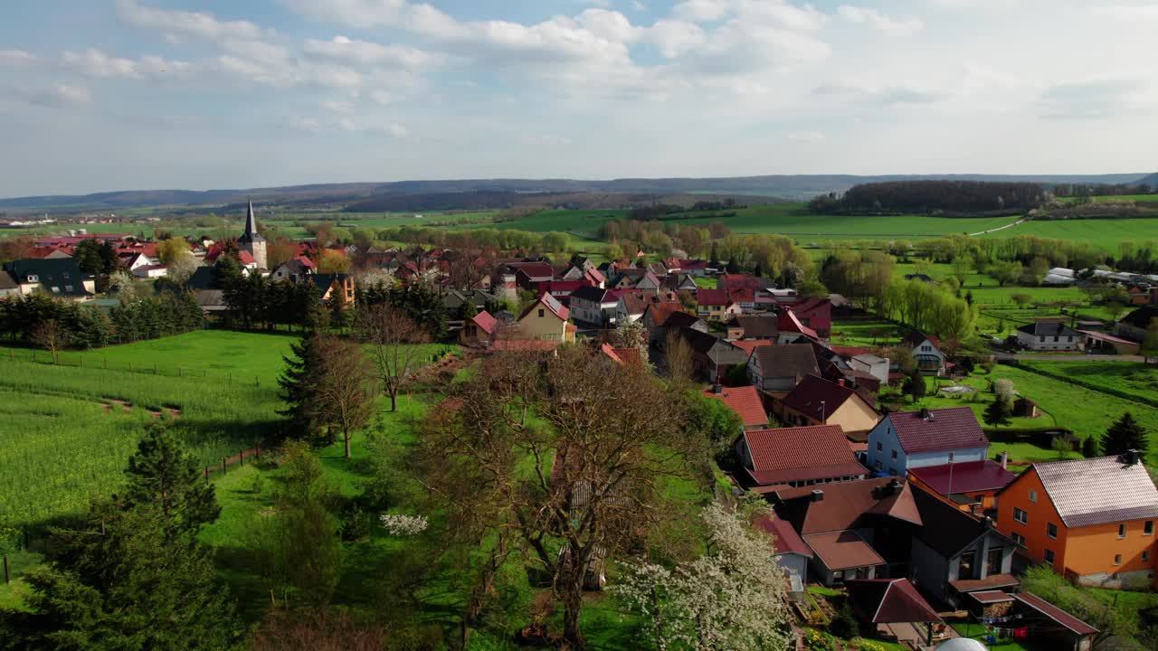 村庄周围环绕着美丽的绿色丘陵景观，日出时色彩斑斓，航拍画面。德国。视频下载
