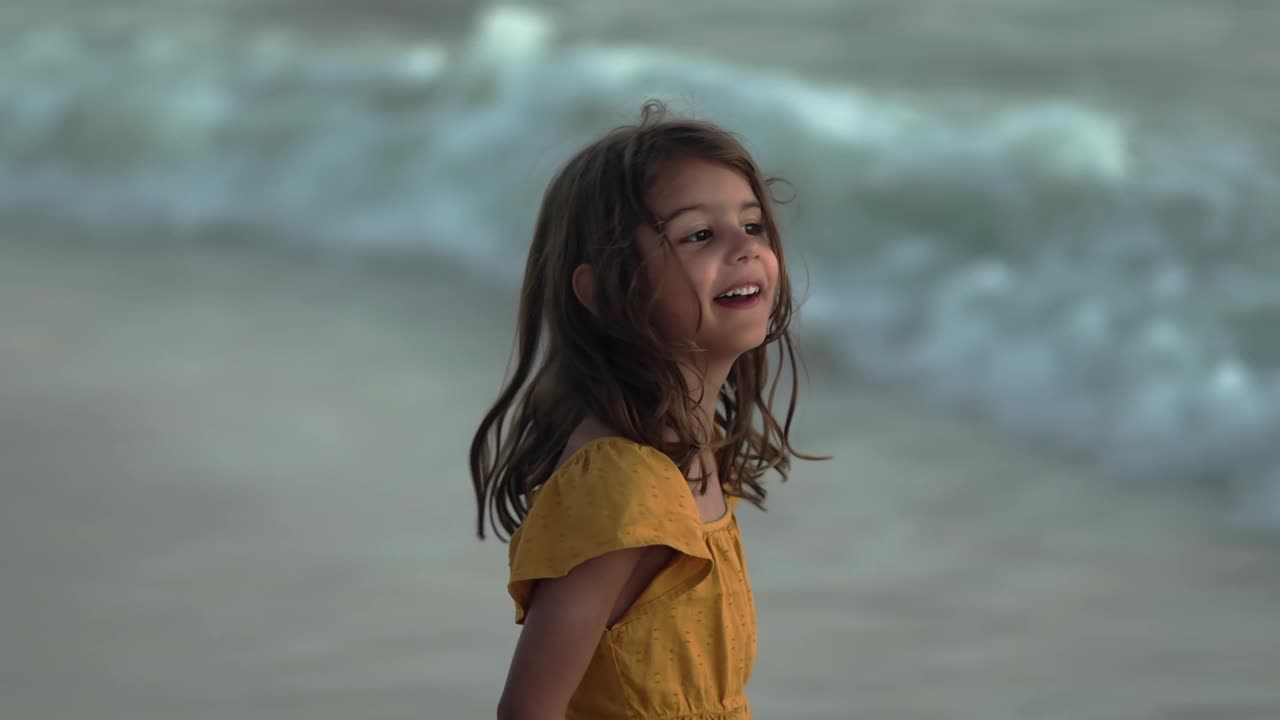快乐的5岁女孩在黄昏的海滩上，海浪滚滚视频下载