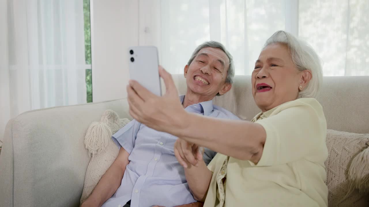 亚洲的老年夫妇喜欢坐在客厅的沙发上玩智能手机视频下载