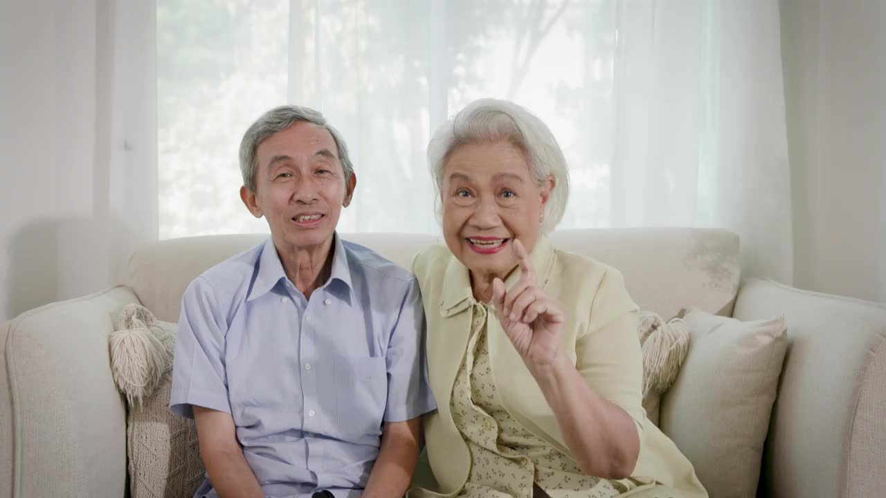亚洲老年夫妇坐在客厅的沙发上，看着镜头的肖像视频下载