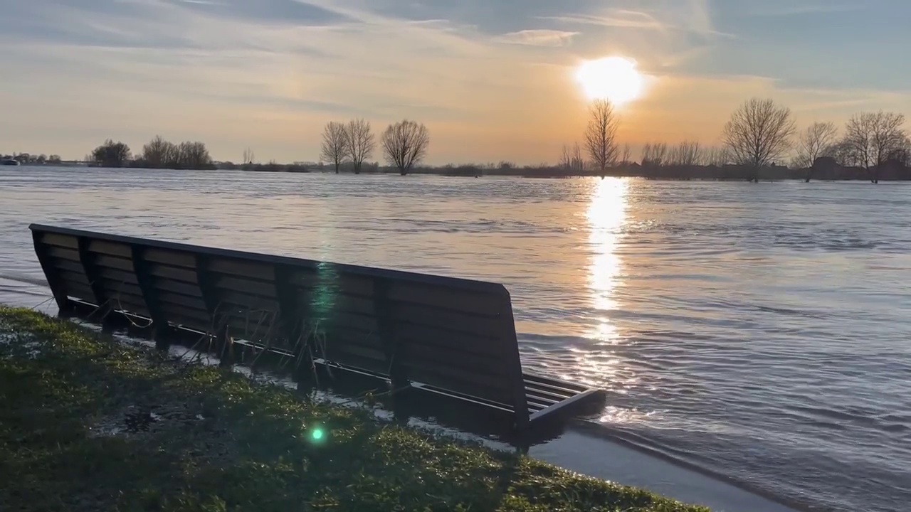 洪水淹没的艾塞尔河的城市林荫大道河床上的波浪在日落时水位上升和高时达到长凳，广阔的洪泛区景观树木在地平线上视频下载