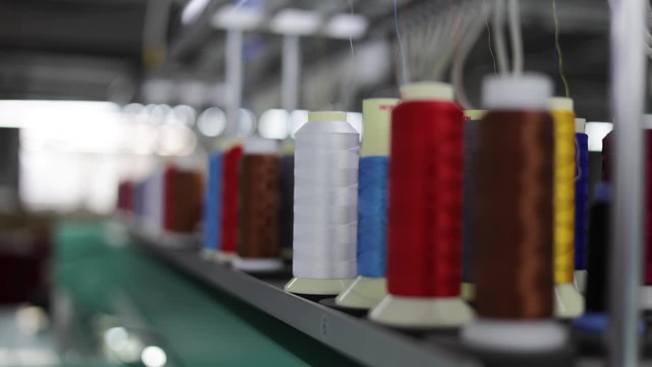 在工业织造机上运行的合成纺织品彩色线卷。选择性关注白色缝纫线轴在纺织织物上的拉伸。生产概念。视频下载