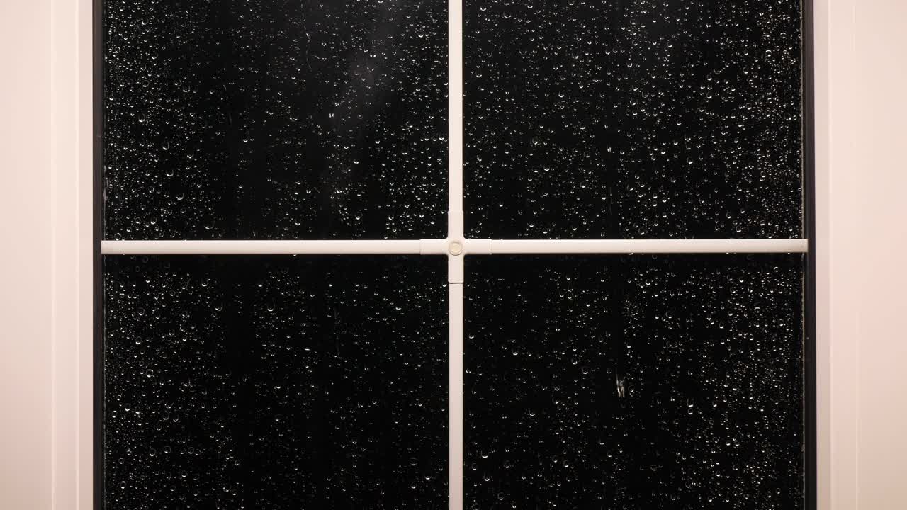 一扇白色的金属塑料窗，夜间有雨点从窗上落下视频素材