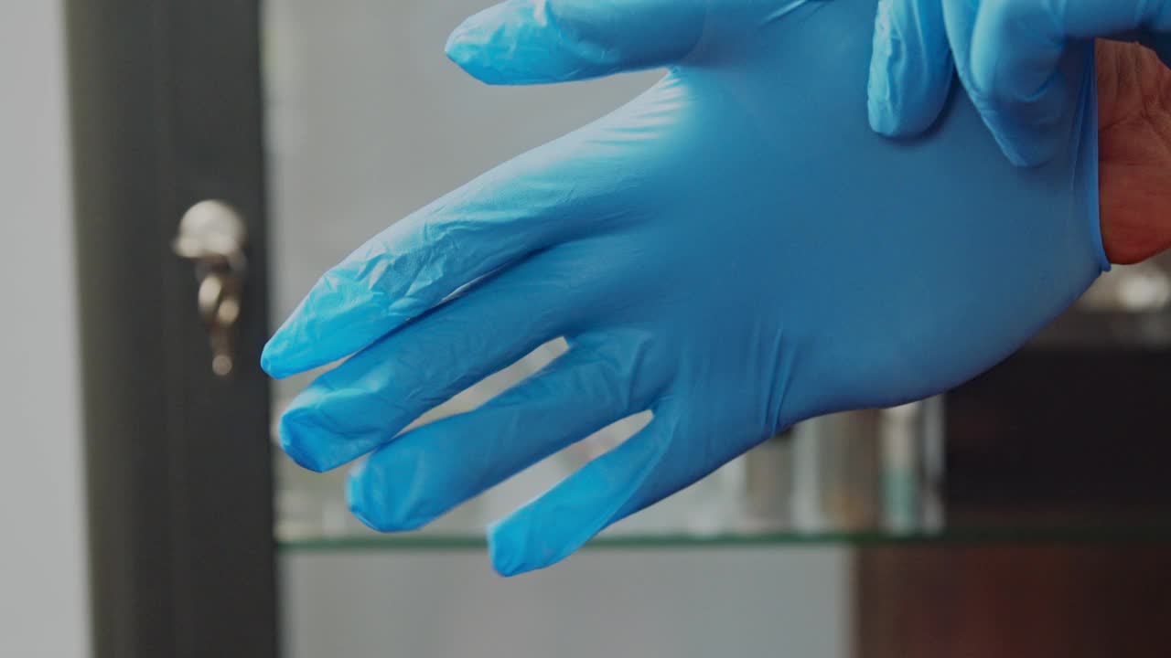 一名男医生戴上蓝色橡胶防护手套。特写镜头视频下载