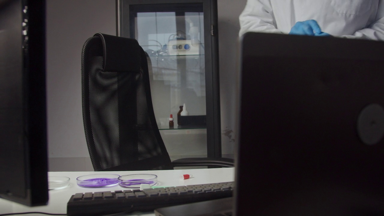 一名身穿白大褂的研究人员使用电脑和培养皿中的化学试剂工作。现代科学家视频下载