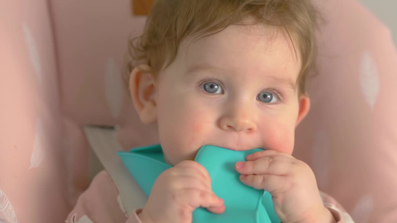 穿着蓝色围兜的婴儿在高脚椅上吃东西和玩耍，4k慢动作60fps视频下载