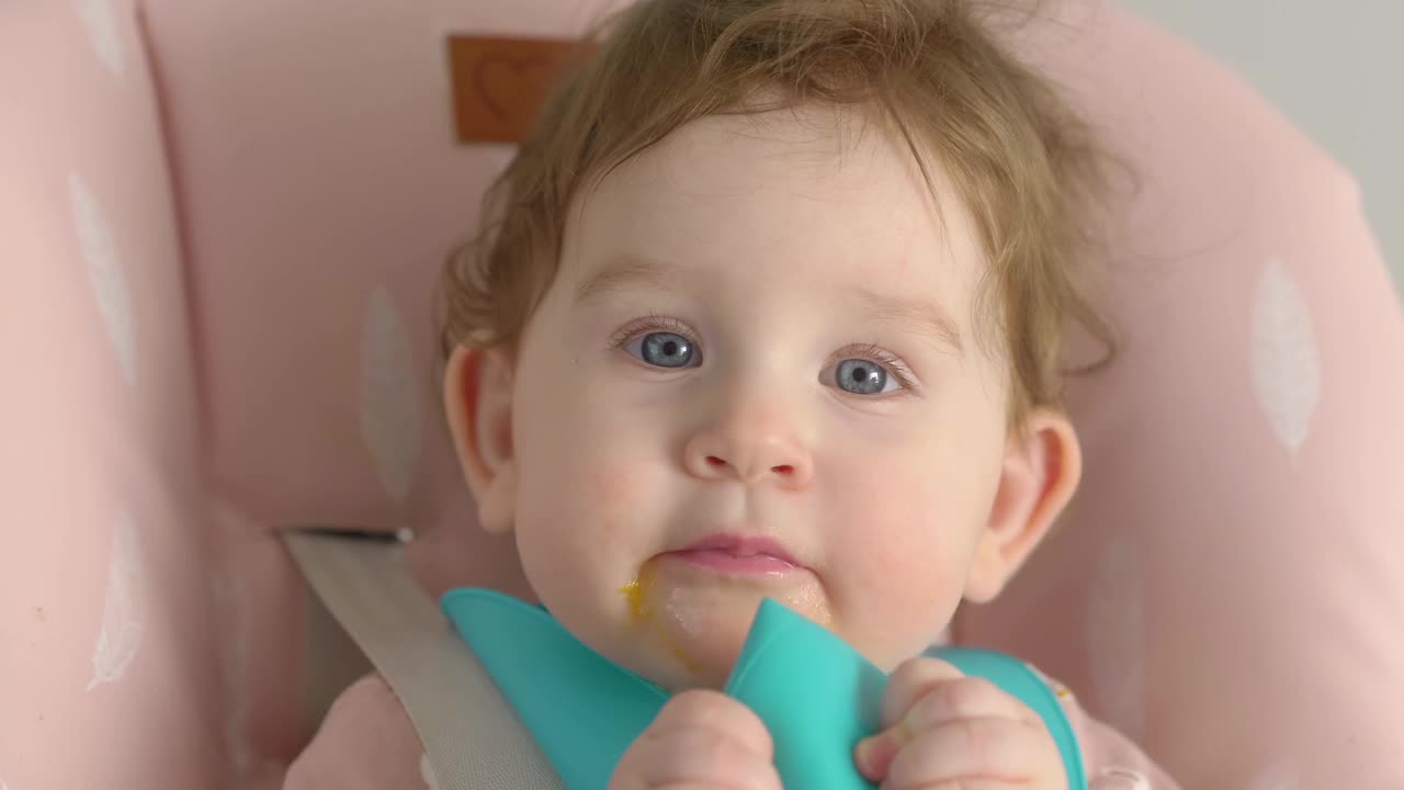 穿着蓝色围兜的婴儿在高脚椅上吃东西和玩耍，4k慢动作60fps视频下载