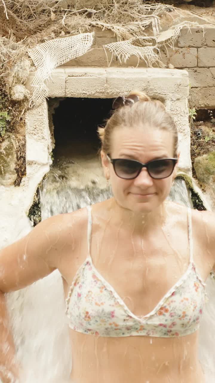 垂直视频。一位年轻女子在克利奥帕特拉温泉池，站在从城墙流出的溪水下。视频下载