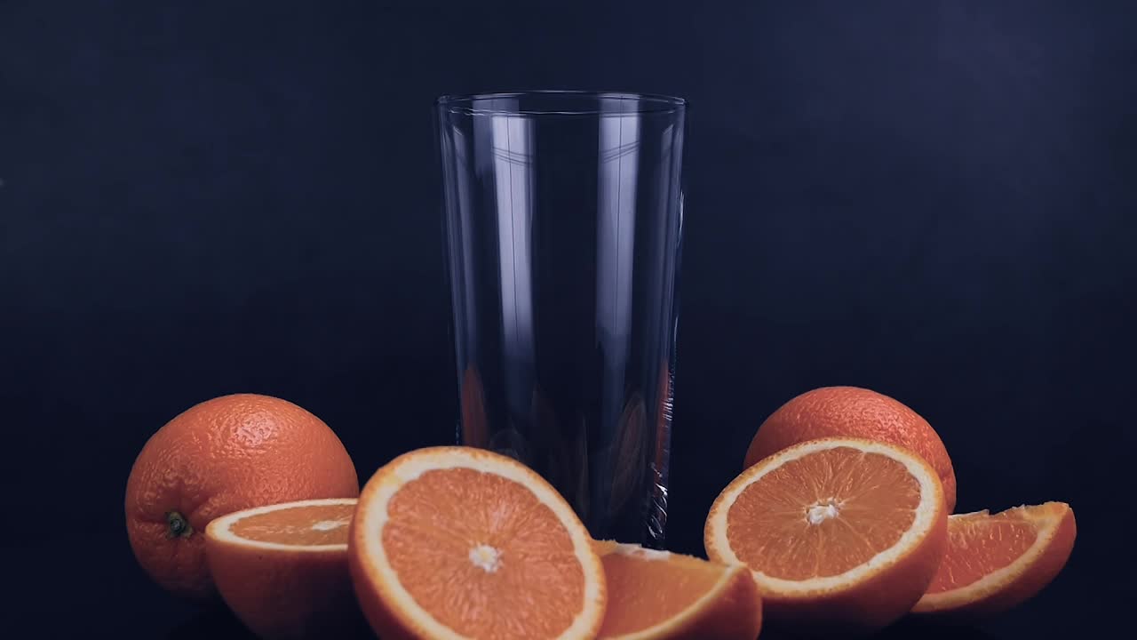 新鲜的橙汁倒进黑色背景的杯子里视频下载