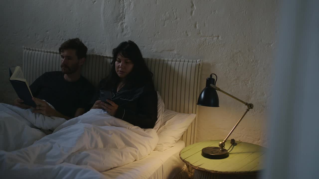 夫妇，晚上和手机在床上阅读，睡前习惯，智能手机和黑暗在家里。浪漫的关系，交流和放松睡觉，晚上和在一起的爱或关心视频下载