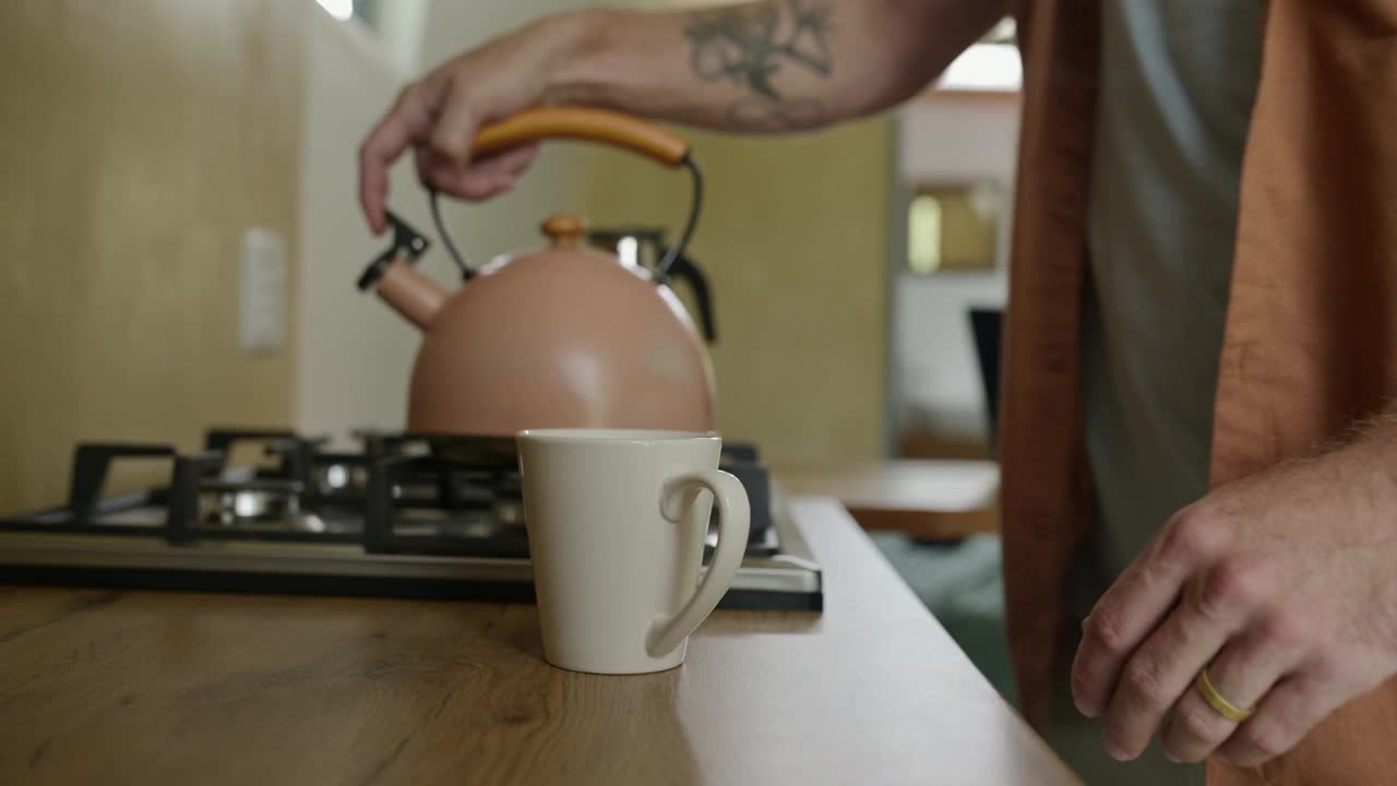 手，水壶和杯子里的水在厨房的柜台上准备，倒或热咖啡。人，燃气设备和炉顶电器在公寓或咖啡，茶或早餐视频下载