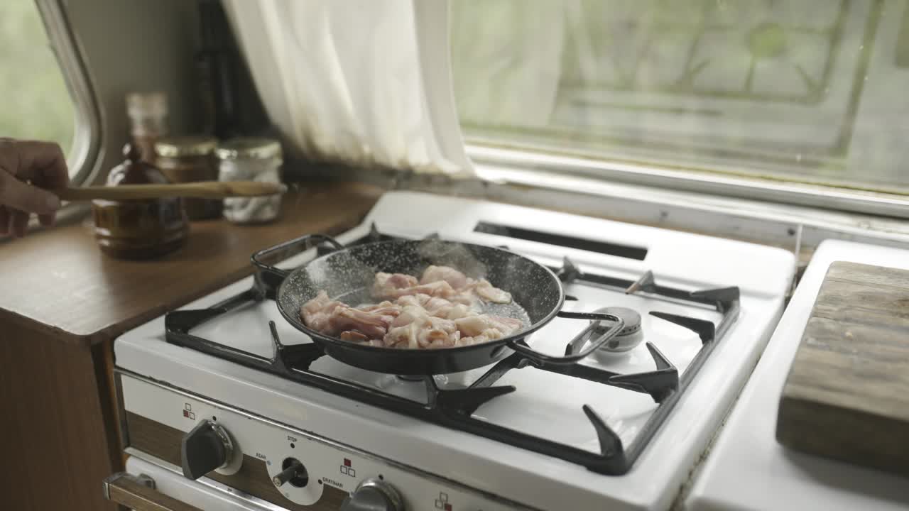在家里的厨房里用煎锅、煎培根和用勺子做早餐。特写，猪肉肉和准备在煤气炉上，健康的蛋白质饮食为营养或吃餐视频下载